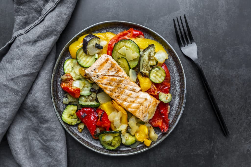 A photo of salmon plated on colorful veggies.